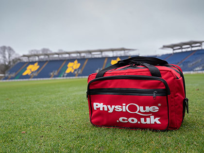 A grass field with a Physique Sports First Aid bag in the forefront