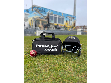 Image of pitchside grassy area with a black Physique first aid bag and a cricket shield on the ground to the right of it